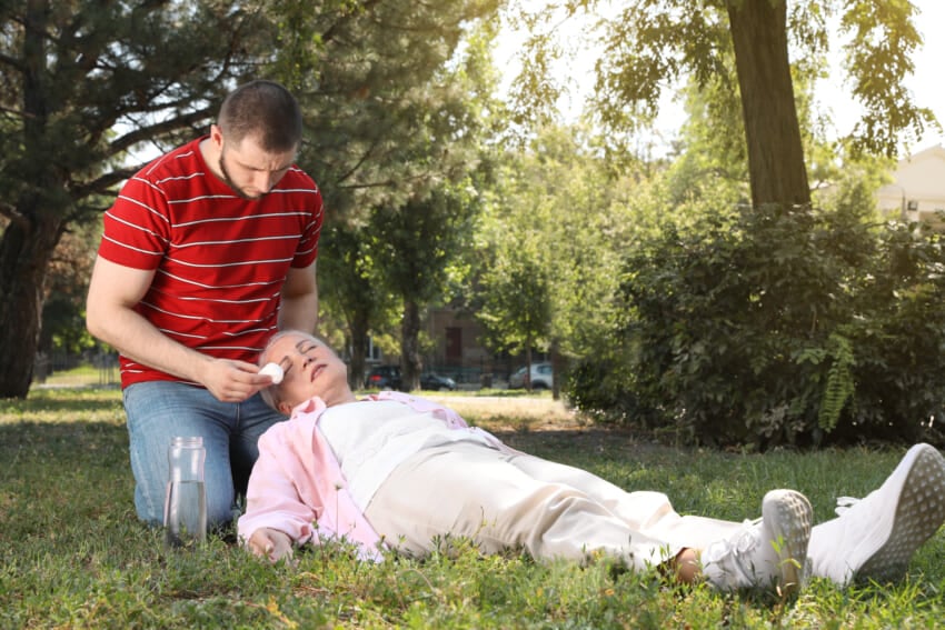 Man-helping-mature-woman-in-park-suffering-from-heat-stroke.jpg