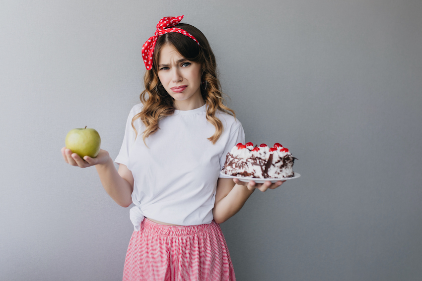 Slim-sad-girl-holding-fruits-and-cake-charming-curly-female-model-can-t-decide-what-to-eat.jpg