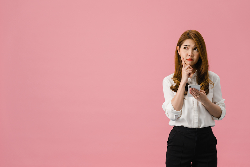 Thinking-dreaming-young-asia-lady-using-phone-with-positive-expression-dressed-in-casual-clothing-feeling-happiness-and-stand-isolated-on-pink-background.jpg