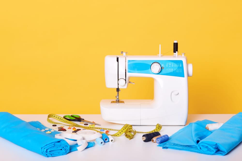 Sewing-equipments-sewing-machine-tap-measure-scissors-pieces-of-cloth-needles-thread-isolated-on-yellow-different-tools-in-sewing-workshop.jpg