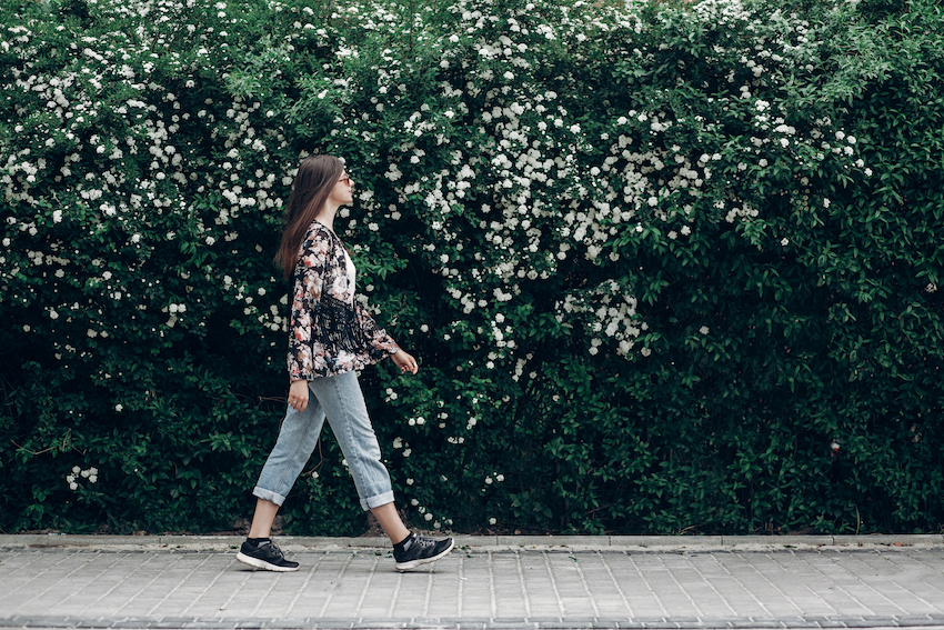 Hipster-woman-in-sunglasses-walking-on-background-of-blooming-bush-with-white-flowers-of-spirea-boho-girl-outing-in-floral-and-denim-modern-clothes-in-summer-city-street-space-for-text.jpg