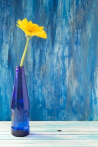 Yellow-gerbera-flower-blue-bottle-wooden-table-against-painted-wall_23-2147874273.jpg