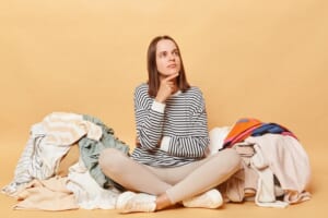 Pensive-thoughtful-woman-sitting-floor-surrounded-by-multicolored-laundry-cluttered-with-clothes-organizing-her-closet-thinking-who-give-unnecessary-outfits-isolated-beige-background_176532-28607.jpg